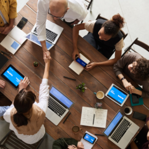 Group of people around table with laptops. 2 are shaking hands