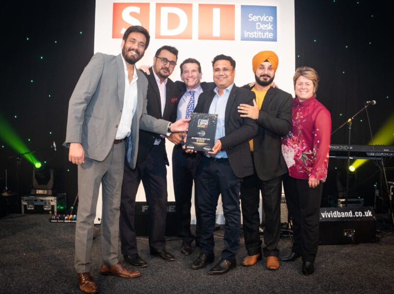 A group of six people, five men and one woman, stand on a stage smiling and holding an award at the SDI Awards 2026. Behind them is an SDI (Service Desk Institute) sign. Everyone is dressed in formal or semi-formal attire.