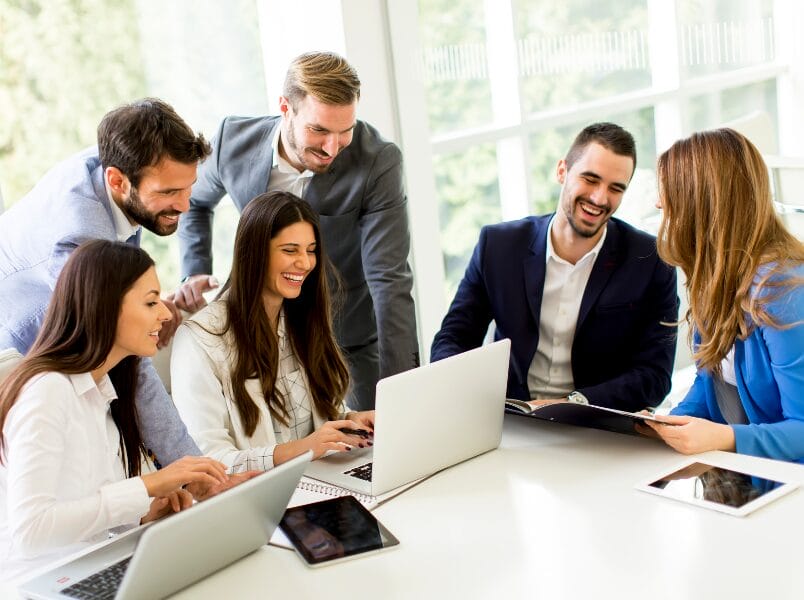 A diverse group of business professionals examines a tablet together, discussing CMDB and collaborating on an Asset Management project.