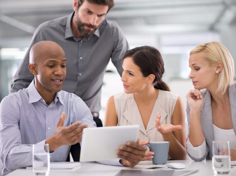 A diverse group of IT professionals collaboratively examining a tablet in a modern office setting.
