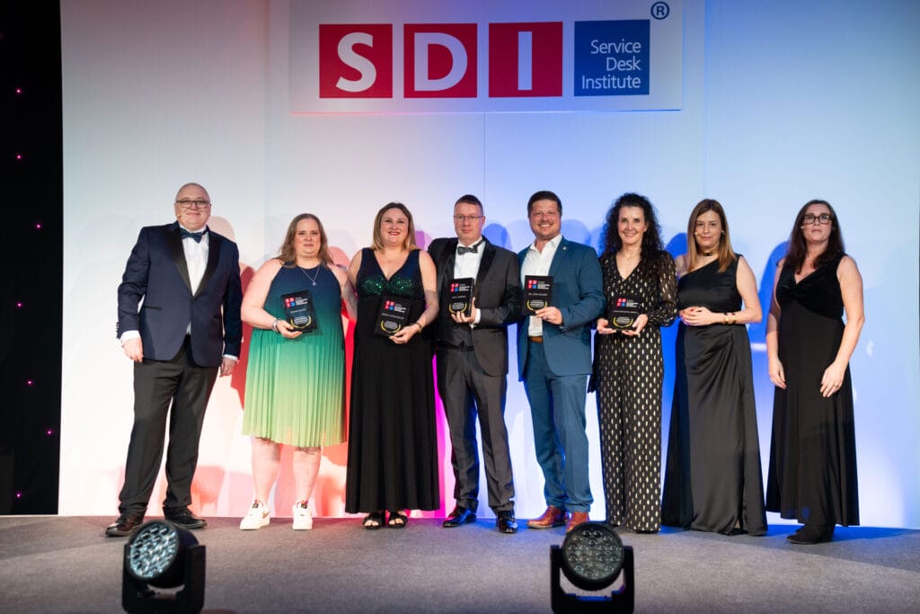 A group of eight industry thought leaders dressed formally stand on stage holding awards, smiling, under a large "SDI Service Desk Institute" sign.